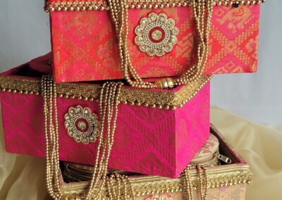 Floral Art presents Three decorative boxes stacked on a wooden surface, each adorned with intricate beaded handles and floral motifs. The boxes are in shades of red, pink, and glimmer with touches of floral jewelry inspiration.