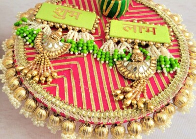 Floral Art presents A decorative platter with green beading, red and pink base, topped with two green rectangular placards and a bangle. Two ornate peacocks are also on the platter, perfect for presenting flower jewelry for haldi or floral bridal jewellery.