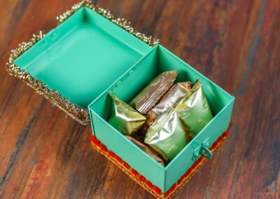 Floral Art presents A teal box with a decorative border is open, revealing several individually wrapped floral bridal jewellery pieces inside, set on a wooden surface.
