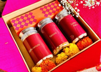 Floral Art presents A delightful gift box featuring jars of cashew nuts, almonds, and spiced pistachios, elegantly arranged with marigold flowers and a pink decorative envelope. Perfectly suited for occasions like a Haldi ceremony, complementing flower jewelry beautifully.