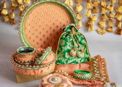 Floral Art presents A collection of decorative gift items, featuring boxes, pouches, and trays in peach hues, adorned with intricate embellishments and tassels. This exquisite set is perfectly complemented by floral jewelry accents against a tassel backdrop.