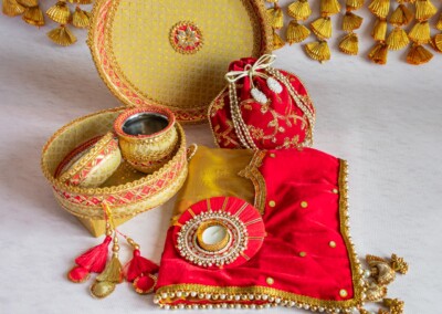 Floral Art presents A decorative set featuring a red fabric, round boxes, a small pouch, tassels, and traditional accessories is elegantly arranged on a light surface, paired with charming floral jewelry perfect for a wedding haldi ceremony.