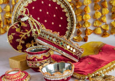 Floral Art presents A collection of decorative Indian wedding items, featuring a red tray, pouches, bowls, and fabric with floral bridal jewellery against a backdrop of tassels.