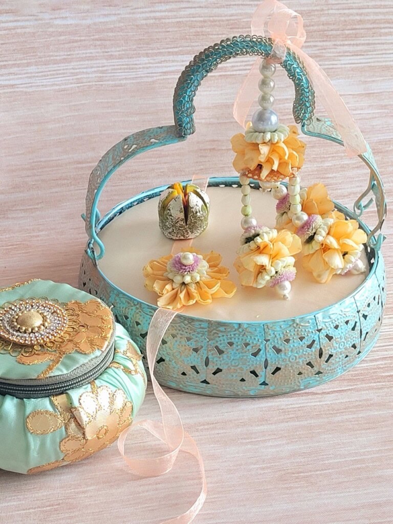 Floral Art presents A decorative blue basket with floral accessories and a drawstring pouch are displayed on a light surface. Fresh yellow orange flowers are also part of the arrangement.