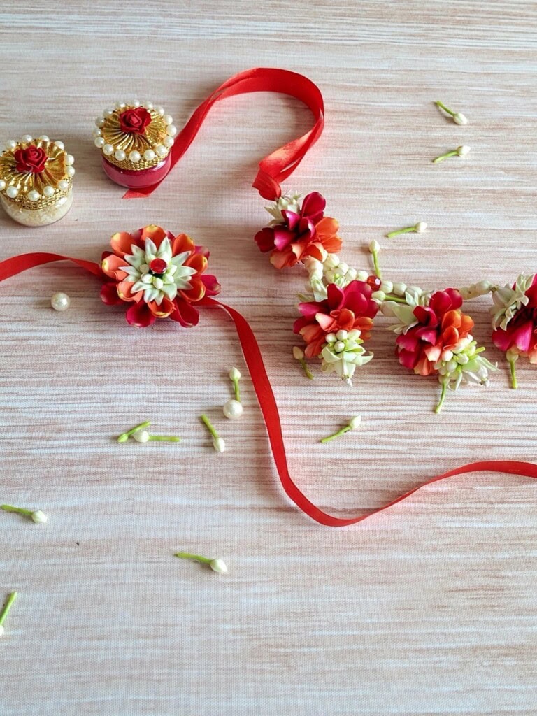 Floral Art presents Red and white flower jewelry set adorned with pearls and a red ribbon is laid out on a light wooden surface. Small buds and pearls are scattered around.