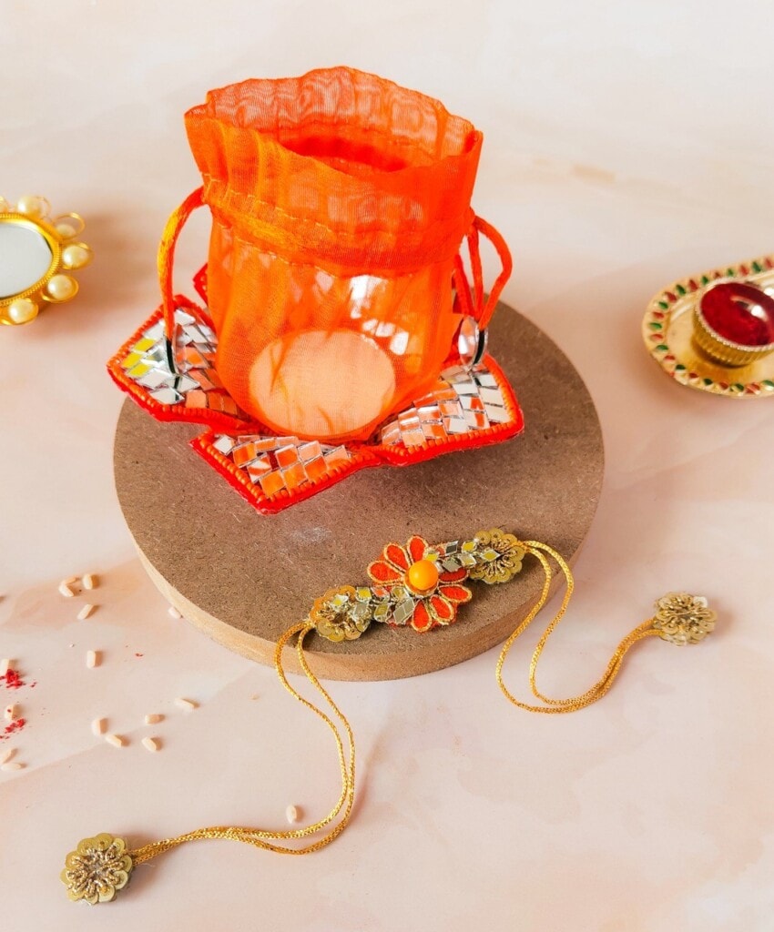 Floral Art presents A decorative orange pouch and a sunflower themed bracelet are displayed on a round platform. Additional small decorative items are placed around the platform.