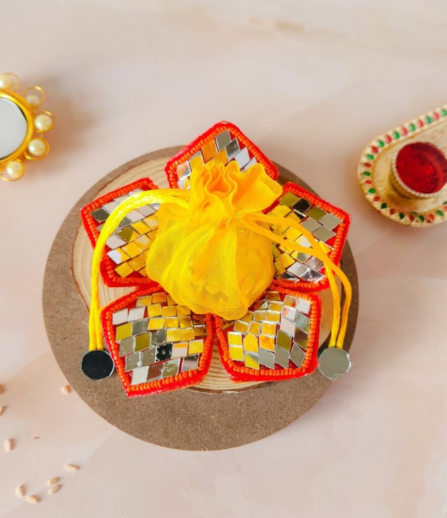 Floral Art presents A decorative, flower shaped item with mirrored tiles and a yellow cloth center on a circular base. Small decorative items are placed nearby on a light colored surface.