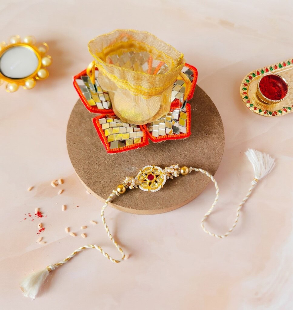 Floral Art presents Decorative items arranged on a surface include a candle holder, a small dish with a red center, and a braided string bracelet. Text reading "floral art" is seen on the surface.