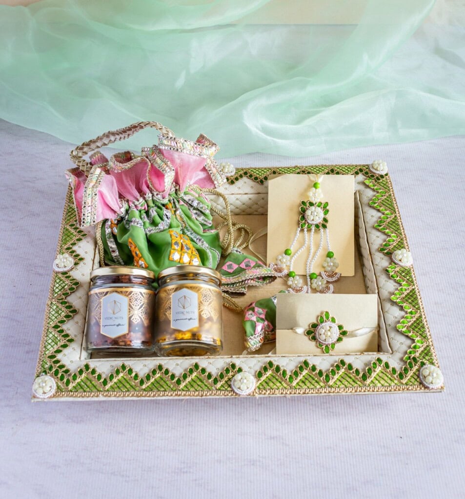 Floral Art presents A decorative tray contains two jars of sweets, green and pink flower bouquets, jewelry, and envelopes, adorned with green and white embellishments. A sheer green fabric is draped in the background.