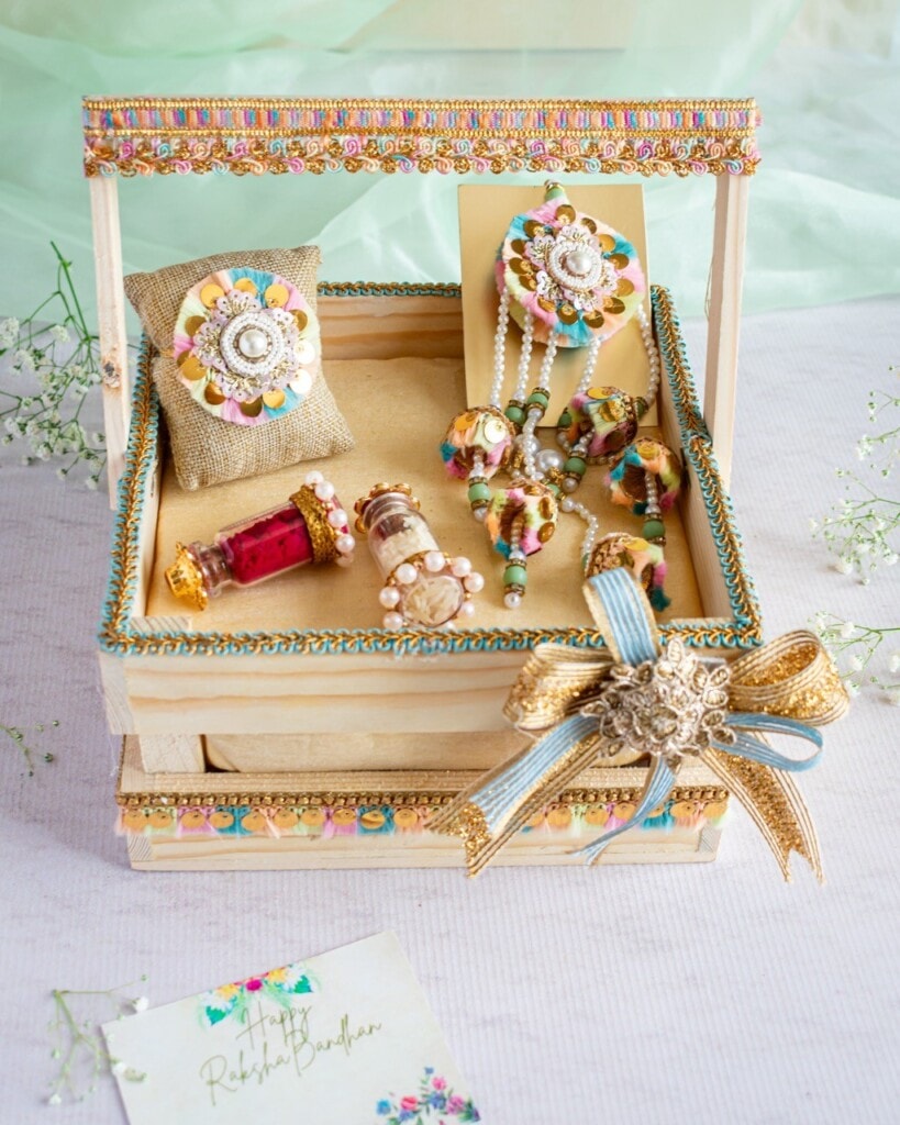 Floral Art presents An ornate jewelry display box contains colorful and intricately designed accessories, including bangles, rings, earrings, and a necklace. A decorated greeting card lies nearby.