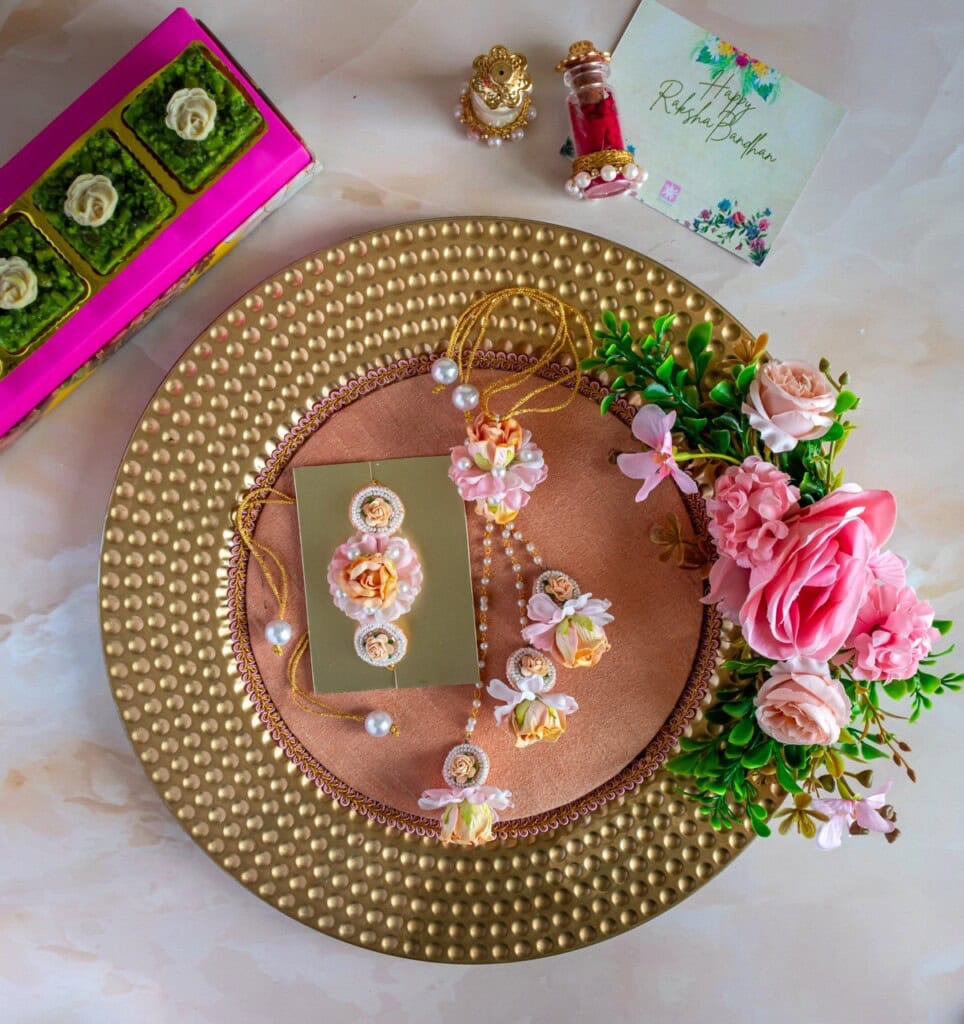 Floral Art presents A decorative tray with artificial flowers and jewelry, including a necklace and earrings, is placed on a textured golden plate. A small bouquet and a card with floral designs are also present.