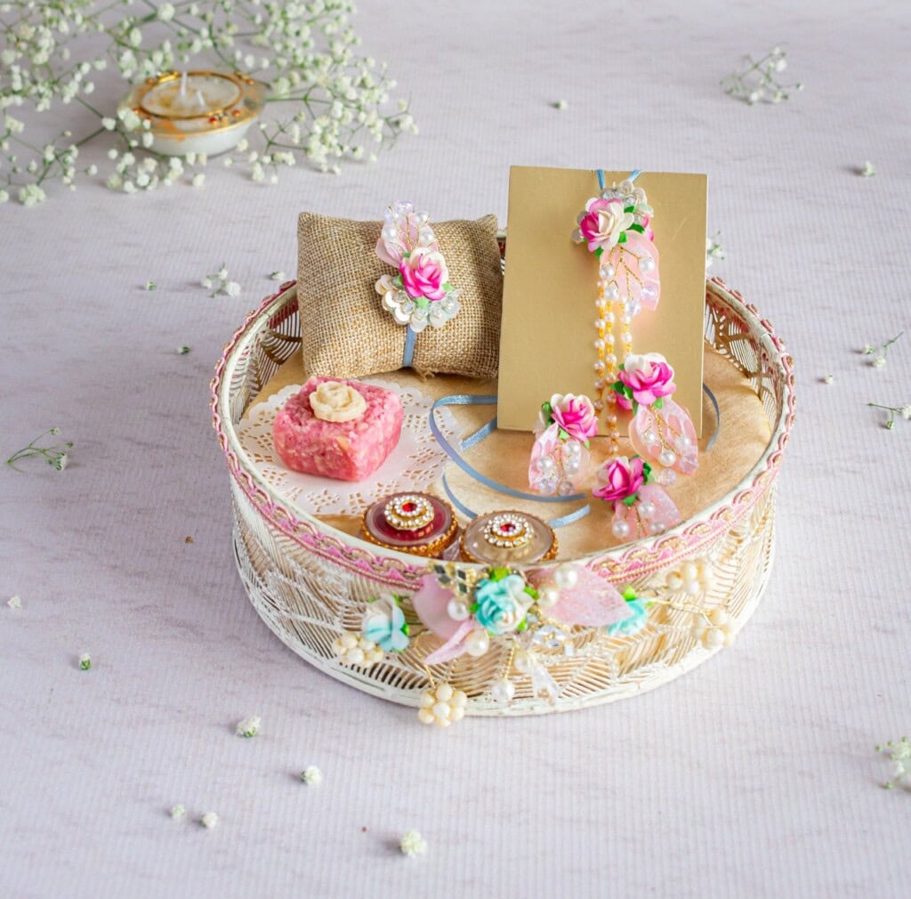 Floral Art presents A decorative basket contains traditional Indian jewelry, flowers, a small pillow, and a card. Baby's breath flowers are scattered around, and a small candle is visible in the background.