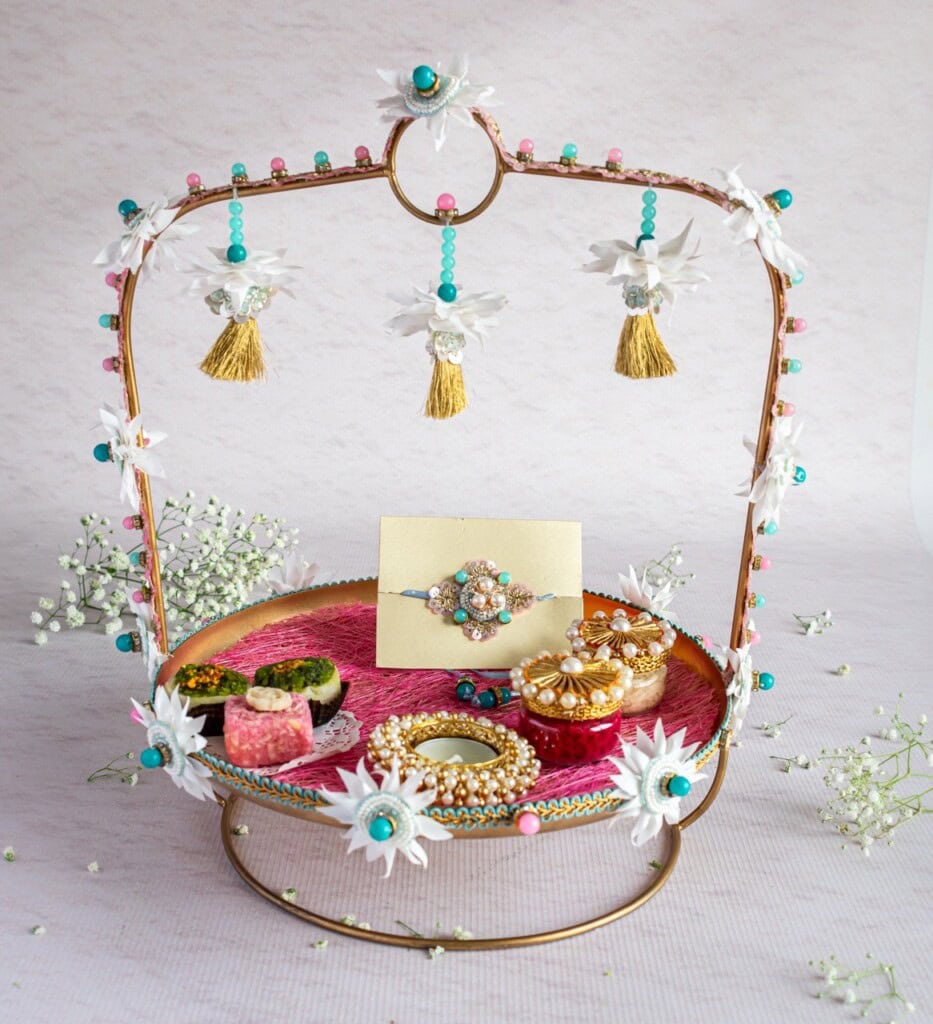 Floral Art presents A decorative tray with floral embellishments holds a jewelry box, sweets, and assorted decorative items. Small white flowers and tassels hang from the frame's arch.