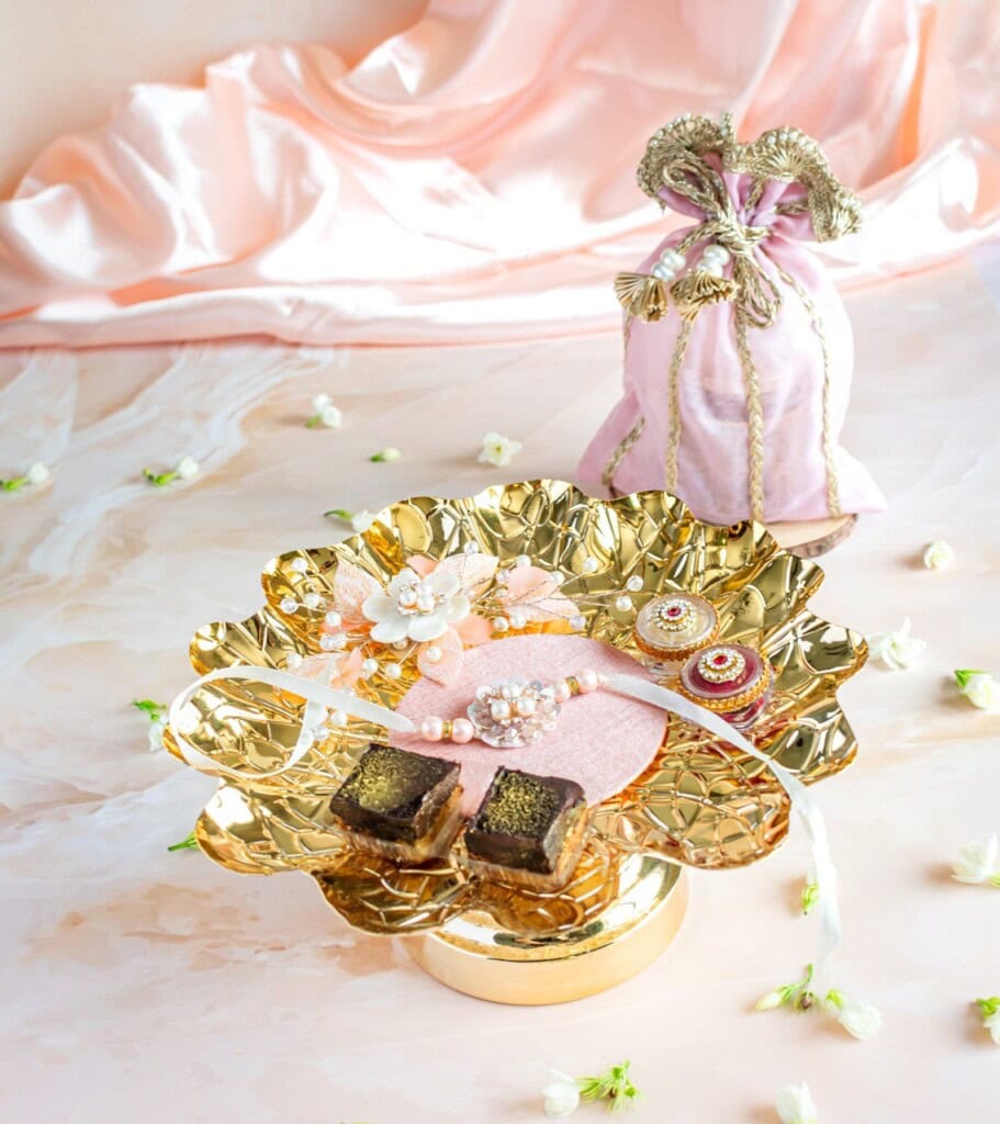 Floral Art presents A decorative golden tray holds assorted chocolates, a beaded bracelet, and small ornate boxes; a pink, embroidered drawstring bag is in the background.