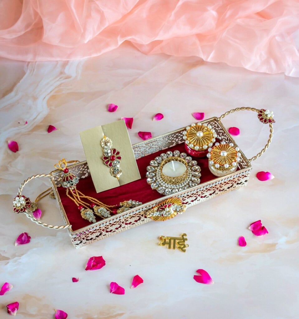 Floral Art presents A decorative tray holding jewelry, a ring, a pair of earrings, and a rakhi bracelet. Scattered pink flower petals surround the tray.