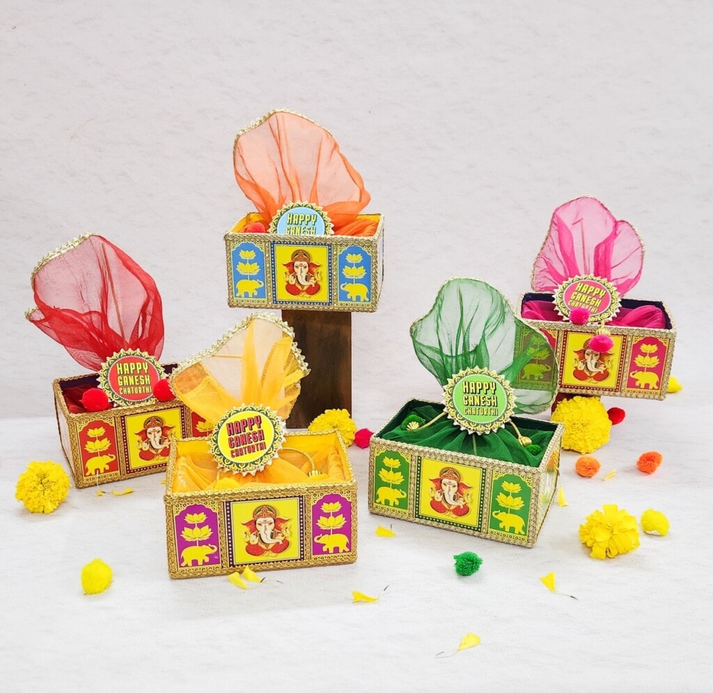 Floral Art presents Colorful gift boxes with "Happy Ganesh Chaturthi" tags, decorated with Pooja items and flowers.