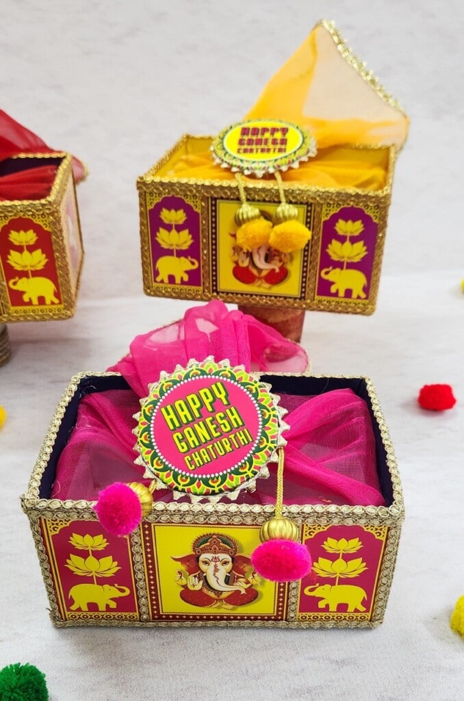 Floral Art presents Decorative boxes with "Happy Ganesh Chaturthi" tags, adorned with colorful fabric and embellishments, and featuring images of Lord Ganesha and traditional motifs.
