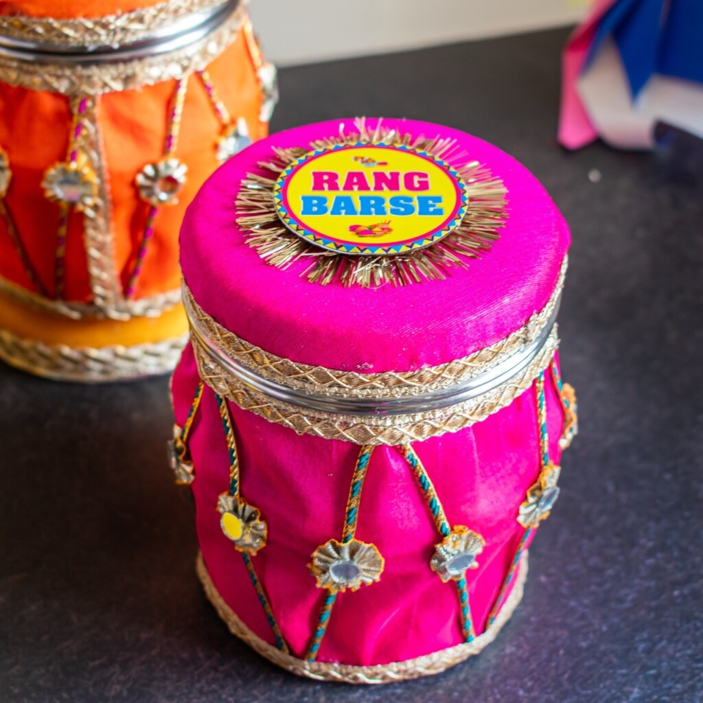 Floral Art presents Decorative container with pink fabric, gold embellishments, and a circular top label reading "Rang Barse.