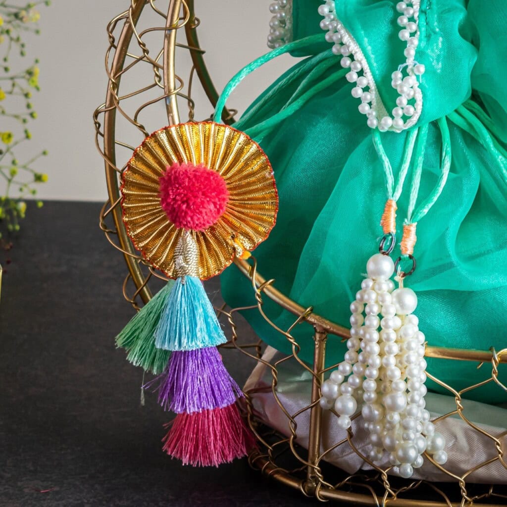 Floral Art presents Colorful tassel ornament hanging on a wire structure with beads and a turquoise fabric backdrop.