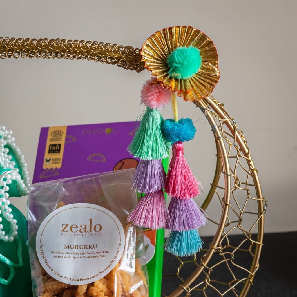 Floral Art presents Decorative basket with tassels and seashells, containing Tafa chocolates and Zealo Murukku snacks, partially wrapped in green fabric.