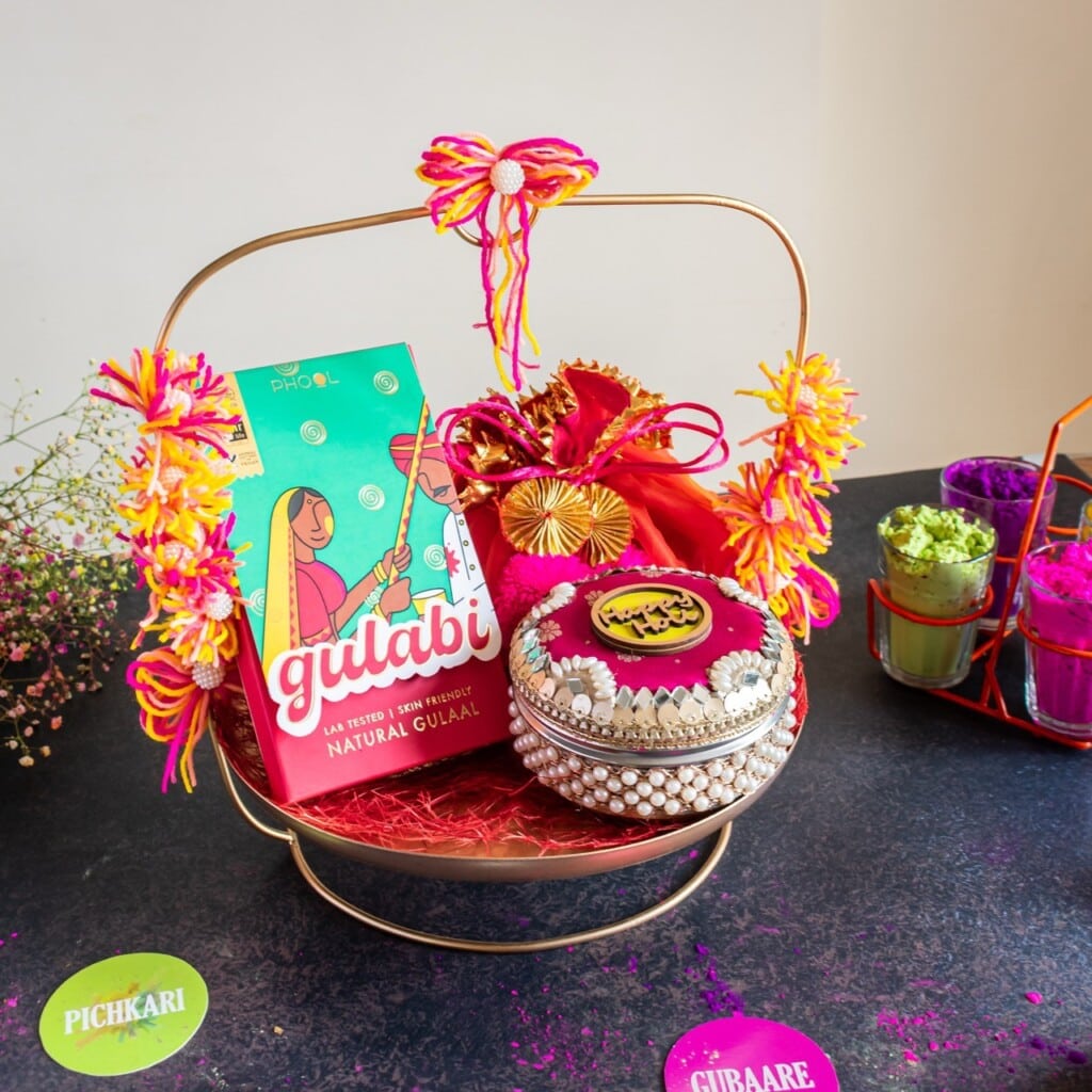 Floral Art presents A festive gift basket with colorful gulal packets, decorated jars, and items adorned with bright flowers.