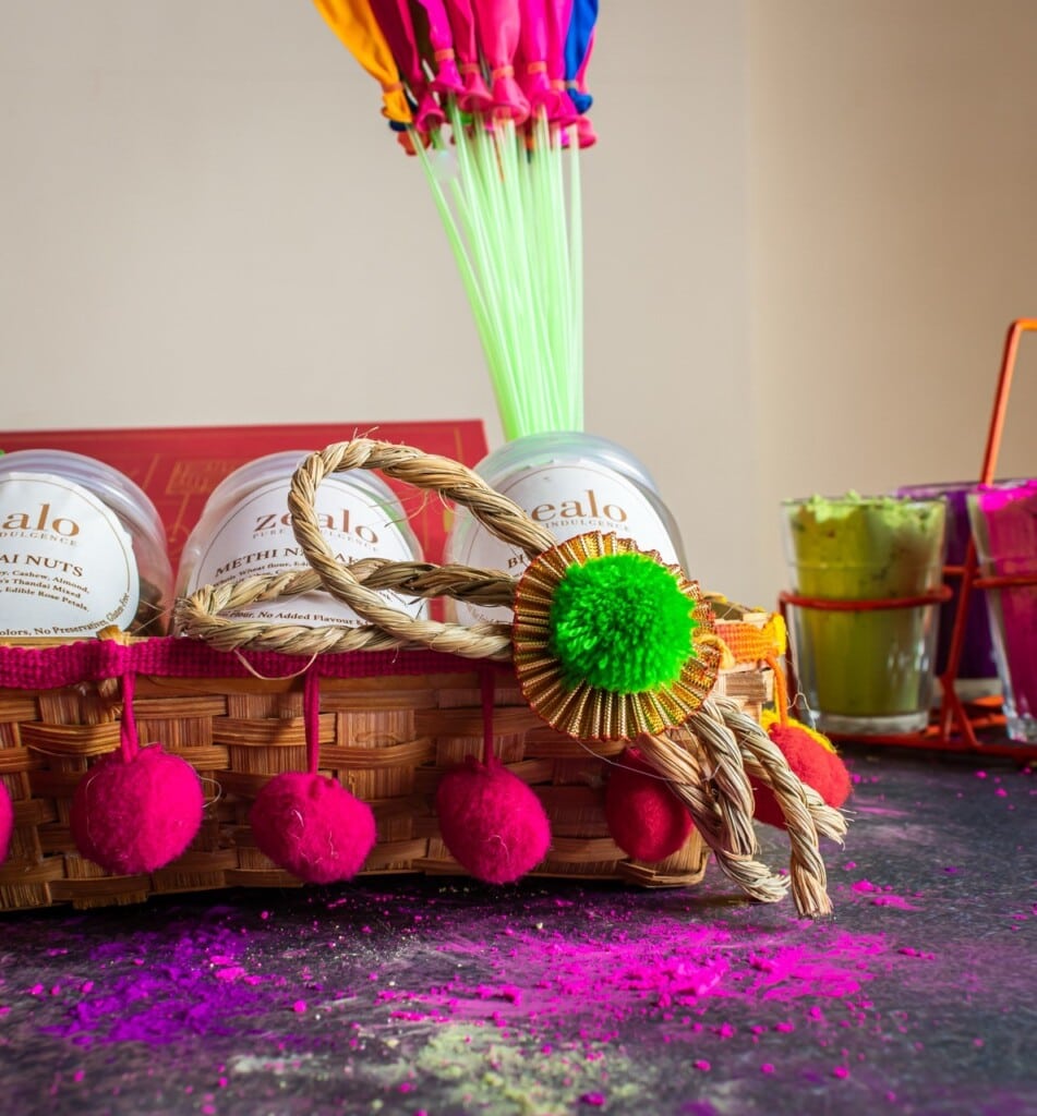 Floral Art presents A basket with snacks and colorful decorations, colored powders scattered on a table, and a bundle of balloons in the background.