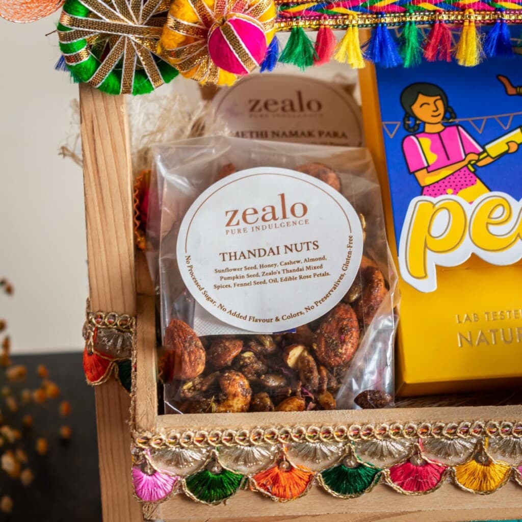 Floral Art presents A wooden tray with a packet of "Zealo Thandai Nuts" and a colorful box, decorated with multicolored fabric and tassels.
