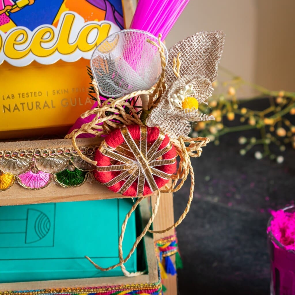 Floral Art presents Decorative items on a shelf, including a red and gold thread ornament and a burlap flower. A colorful package with partial text in the background.