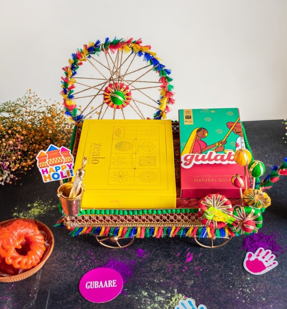 Floral Art presents A decorative tray with colorful gulal packets, a Holi themed sign, and floral decorations.