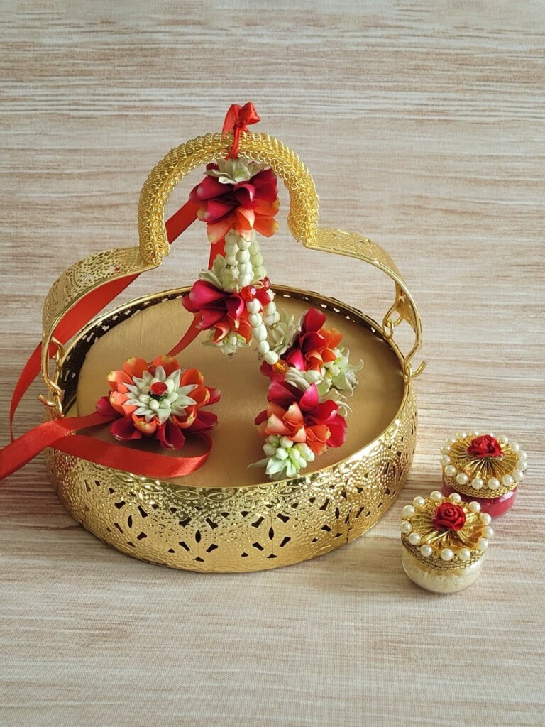 Floral Art presents A decorative gold tray with floral jewelry and two small containers adorned with pearls and artificial red flowers, set on a wooden surface.