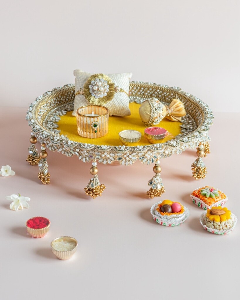 Floral Art presents A decorated tray with jewelry, a cushion, and sweets, adorned with beads and tassels, placed on a light surface with small flower and sweet arrangements nearby.