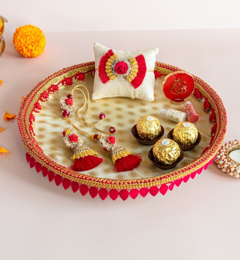 Floral Art presents A decorated tray with traditional jewelry, chocolates, a small mirror, wrapped gifts, and religious items, set on a light surface with a marigold flower nearby.