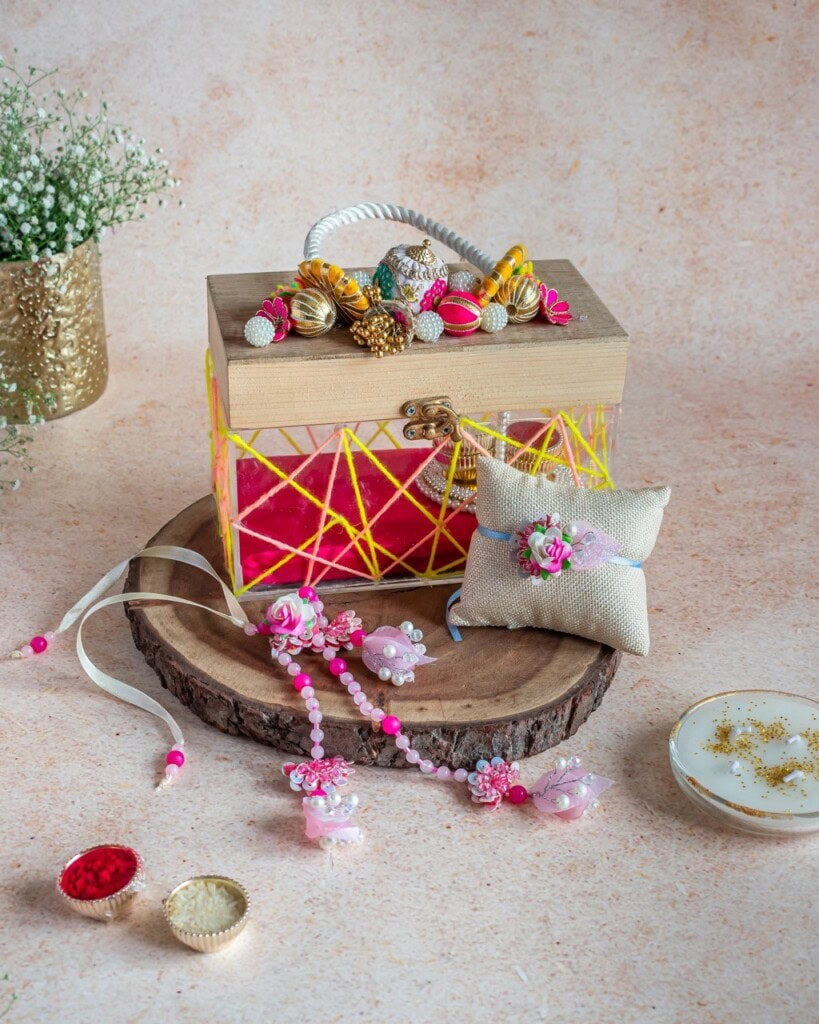 Floral Art presents A decorated wooden box with floral accents sits on a wooden platter, surrounded by a beaded necklace, a cushion, cups with colored powders, a candle, and a gold vase with white flowers.