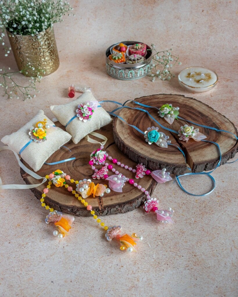 Floral Art presents A display of colorful handmade floral themed jewelry and accessories, including bracelets and brooches, arranged on wooden slices with decorative cushions and containers.