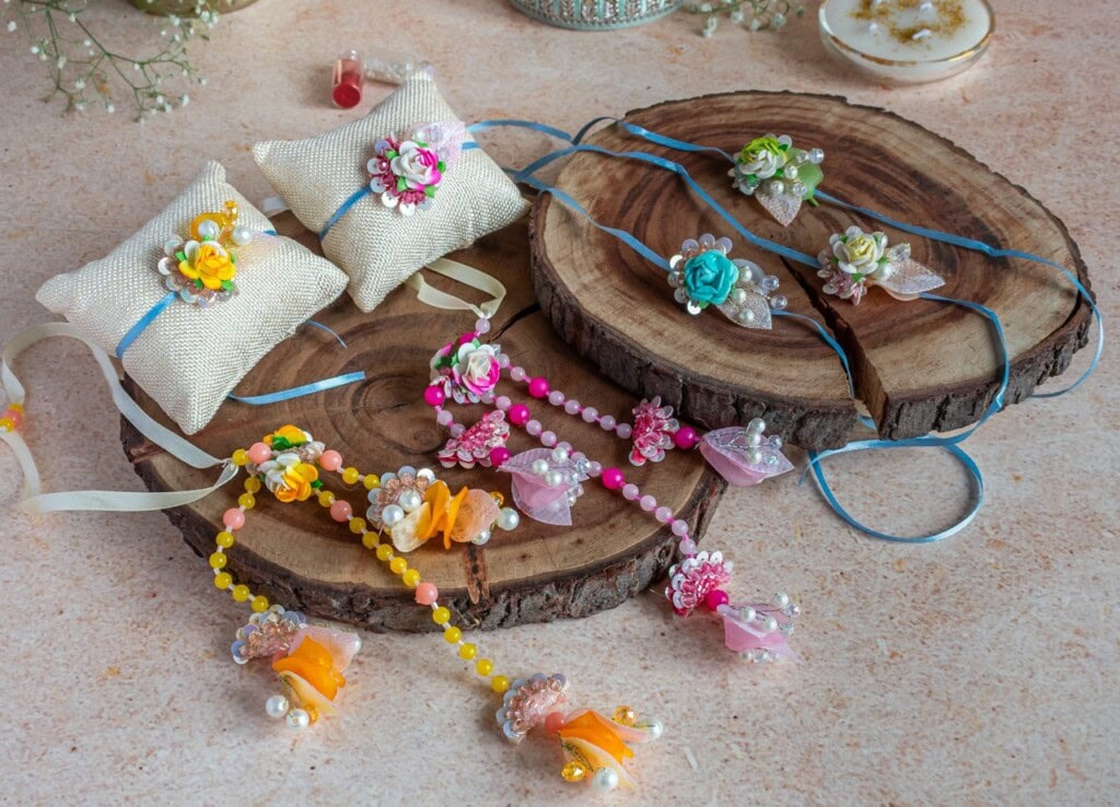 Floral Art presents Handmade floral rakhis and accessories with colorful artificial flowers and beads are displayed on wooden slices and fabric cushions.