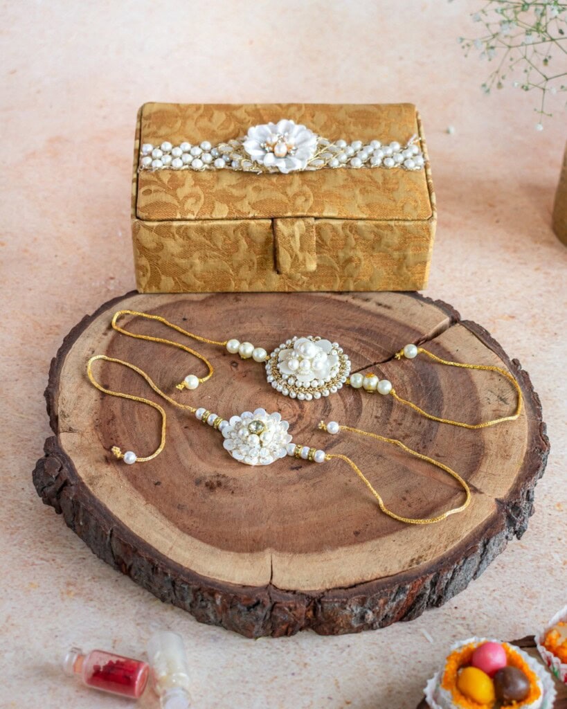 Floral Art presents A gold and white jewelry set with floral designs is displayed on a wooden slab, with a matching decorative box in the background.