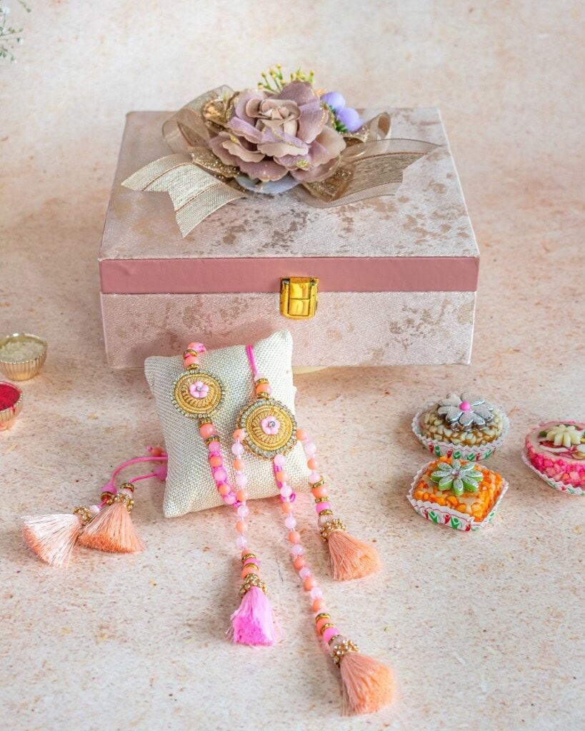 Floral Art presents A decorative box with a flower ornament, two beaded and tasseled bracelets, and small decorative containers arranged on a light surface.