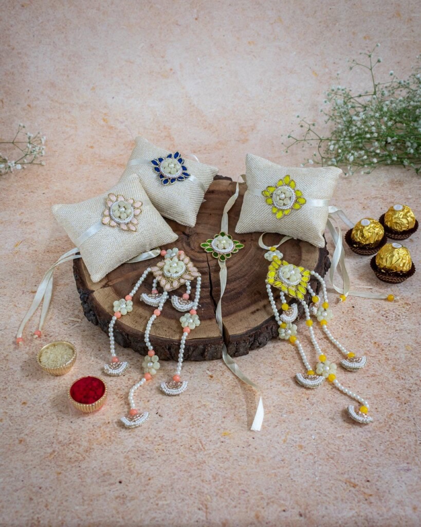 Floral Art presents Three decorative pillows on a wooden tray display colorful beaded rakhis with attached embellishments, surrounded by small sweets and a bowl of red powder.