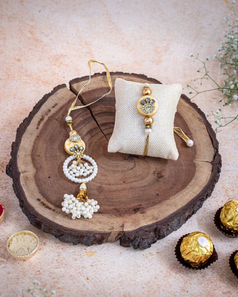 Floral Art presents Traditional Rakhi and a beaded bracelet displayed on a wooden slab with chocolates and a decorative pillow, set against a light background.