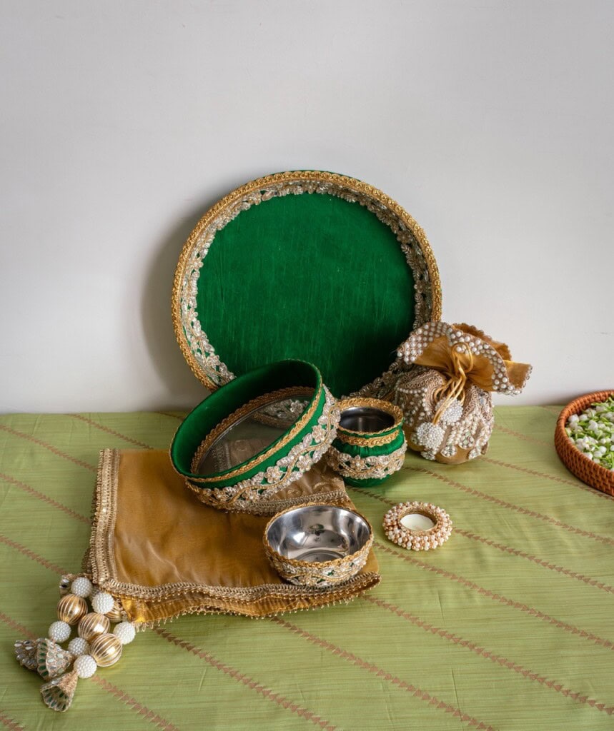 Floral Art presents A decorative green and gold tray set with embellished bowls, a fabric pouch, a napkin with tassels, and a round accessory on a green patterned cloth.