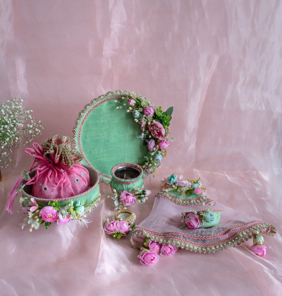 Floral Art presents A decorative pink and green gift tray set with floral embellishments, a pouch, jewelry, cups, and a small pot, arranged on a pink cloth background.