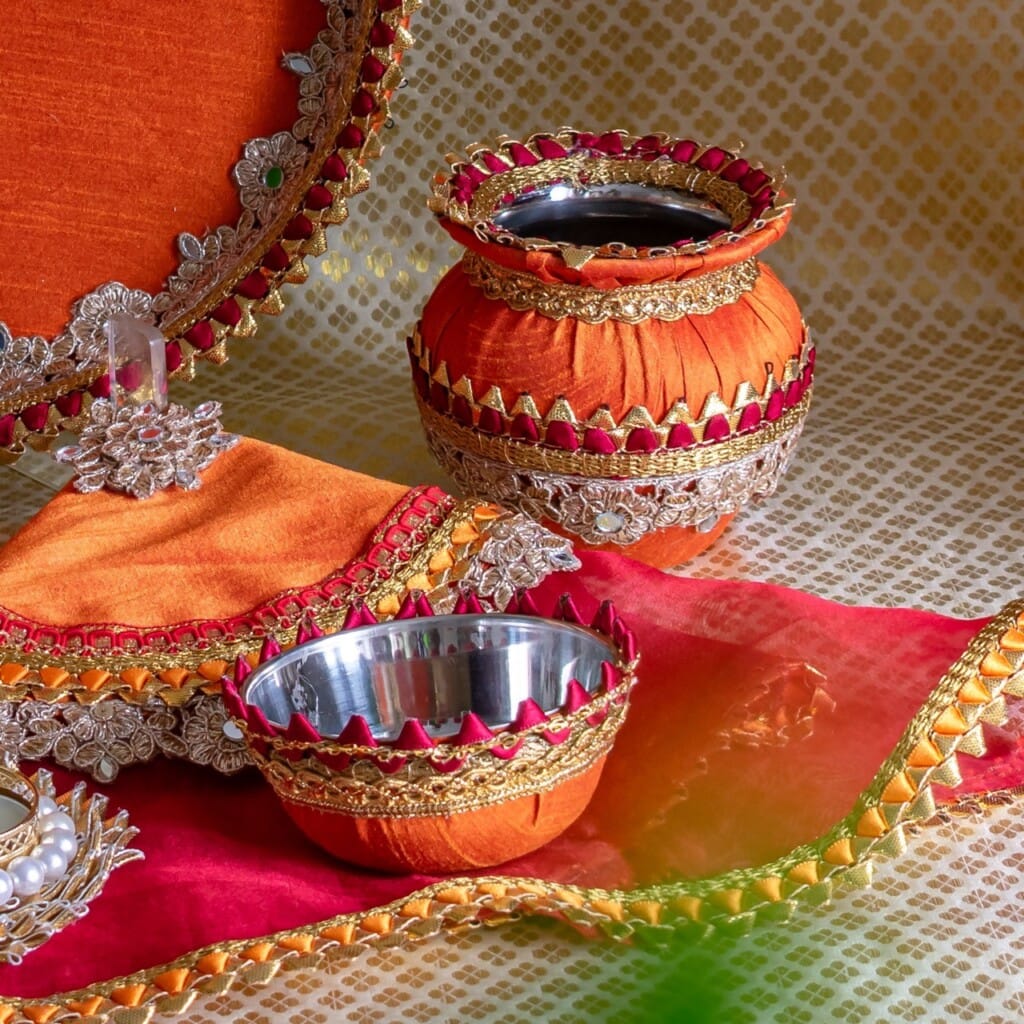 Floral Art presents Decorative metal bowls and pots covered in orange and red fabric with gold accents, arranged on a patterned surface.