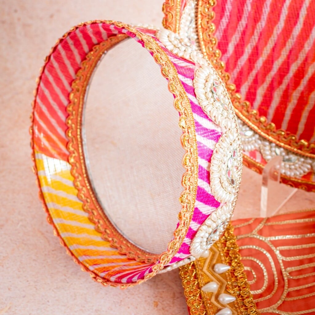 Floral Art presents A close up of a decorative pink, orange, and gold bangle with white beads and intricate embroidery, set against a matching textile background.