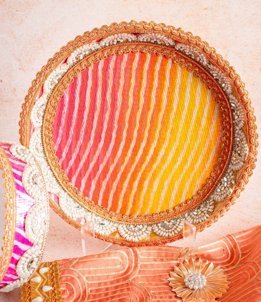 Floral Art presents A decorative round tray with orange, yellow, and white stripes, adorned with gold and beaded trim, displayed against a light background.