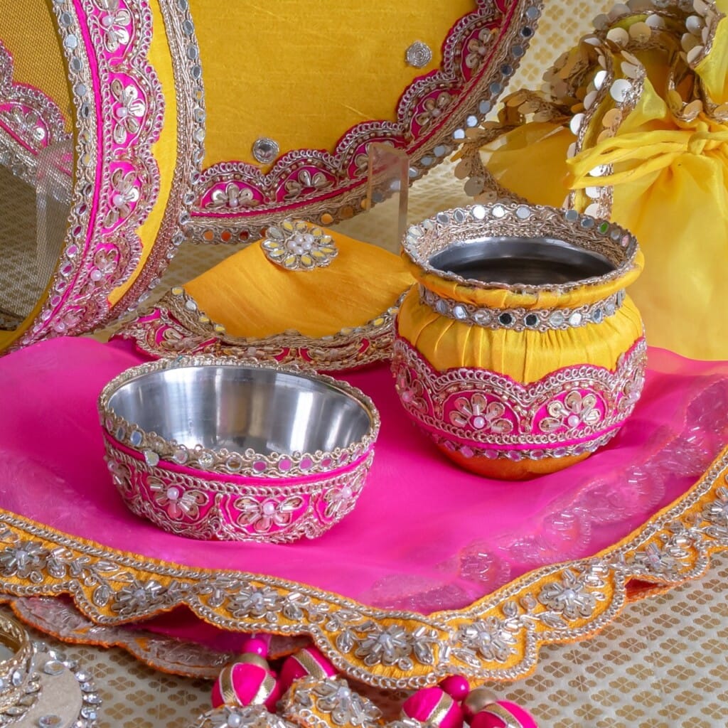 Floral Art presents Decorative metal bowls and jars with pink, yellow, and silver embellishments arranged on a matching tray with embroidered fabric.
