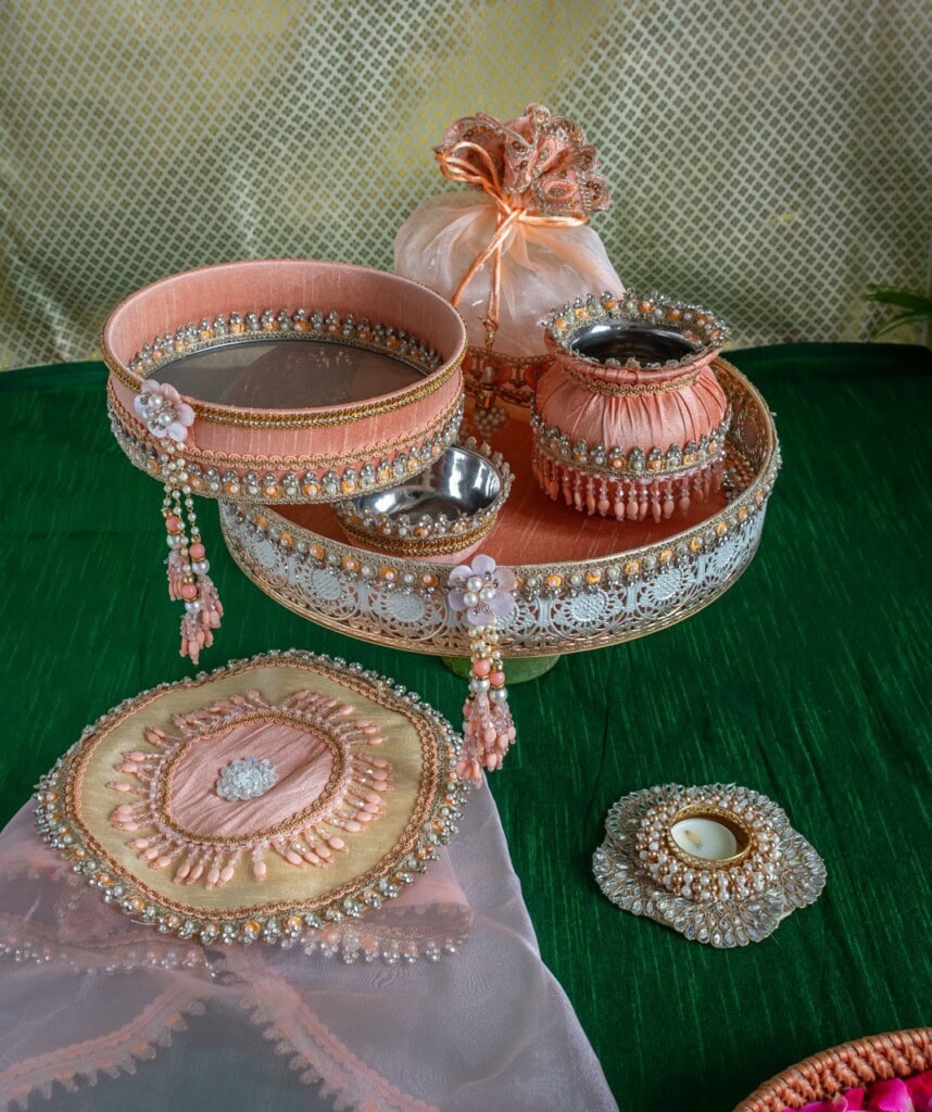 Floral Art presents A decorative tray with beaded bangles, a small jar, a pouch, a tealight holder, and a cloth pouch, all in coordinated pink and gold, displayed on a green surface.