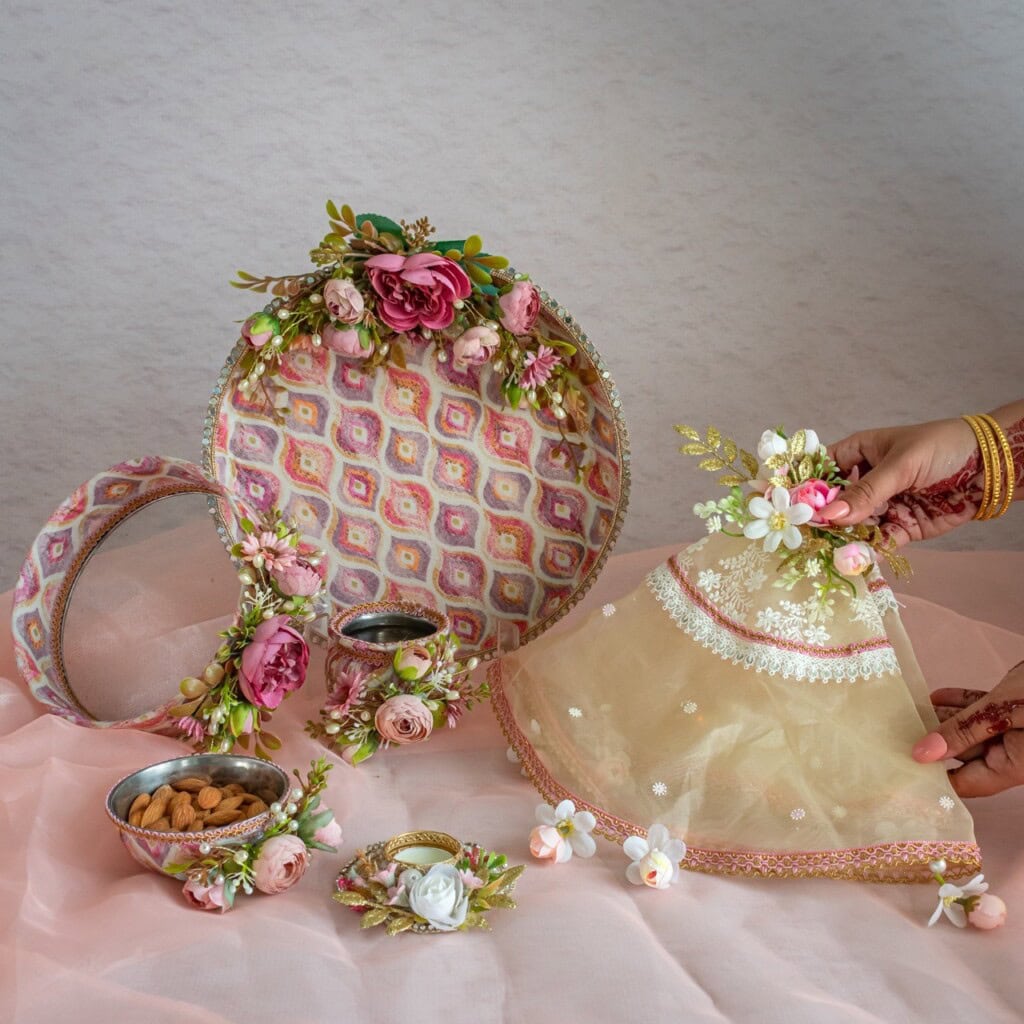 Floral Art presents Decorated trays, bowls, and a sieve with floral accents, nuts, and a veil adorned with flowers, used in a traditional ceremony. Two hands hold the veil and sieve.