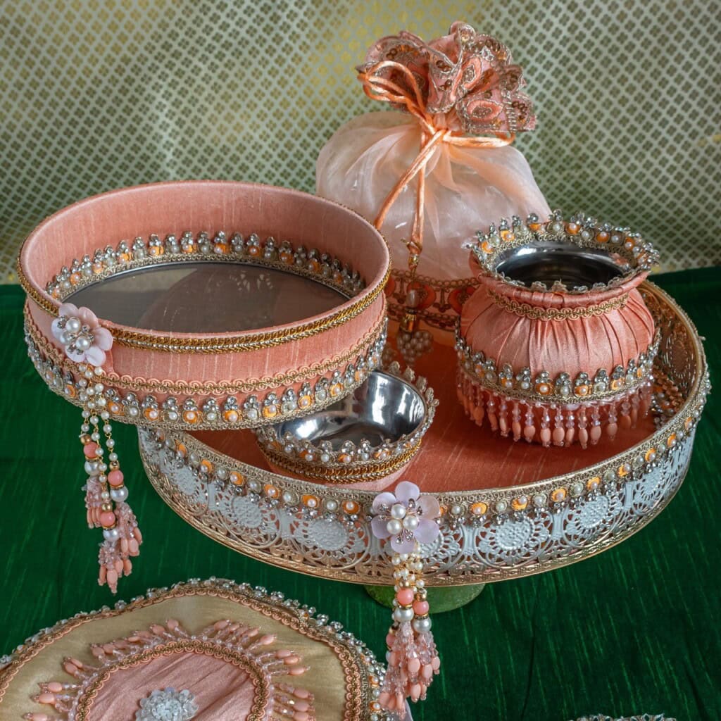 Floral Art presents Decorative trays and containers adorned with pink fabric, beads, and lace, displayed on a green surface with a gift pouch in the background.