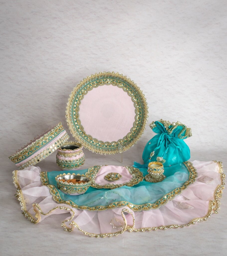 Floral Art presents A decorative set of pink and turquoise embroidered items, including trays, containers, a pouch, and a cloth with gold trim, displayed against a light background.