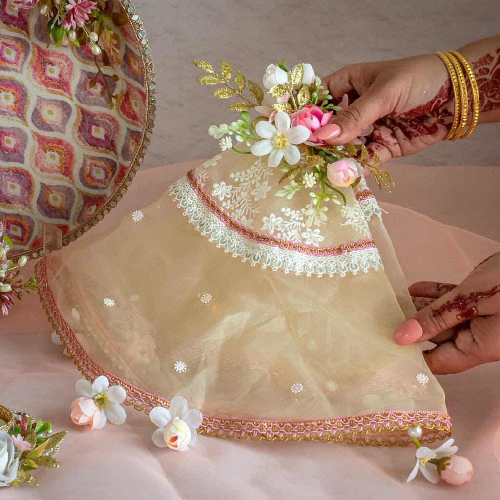Floral Art presents Two decorated hands hold a sheer, floral embroidered cloth with lace and flower embellishments, next to a round tray and more flowers.